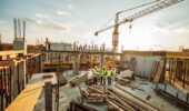 Construction industry concept - architects and engineers discussing work progress between concrete walls, scaffolds and cranes.