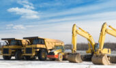 Dump trucks, steam roller & excavators sitting on a construction site in winter.