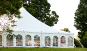 a white wedding tent set up in a lawn surrounded by trees and with the sides down